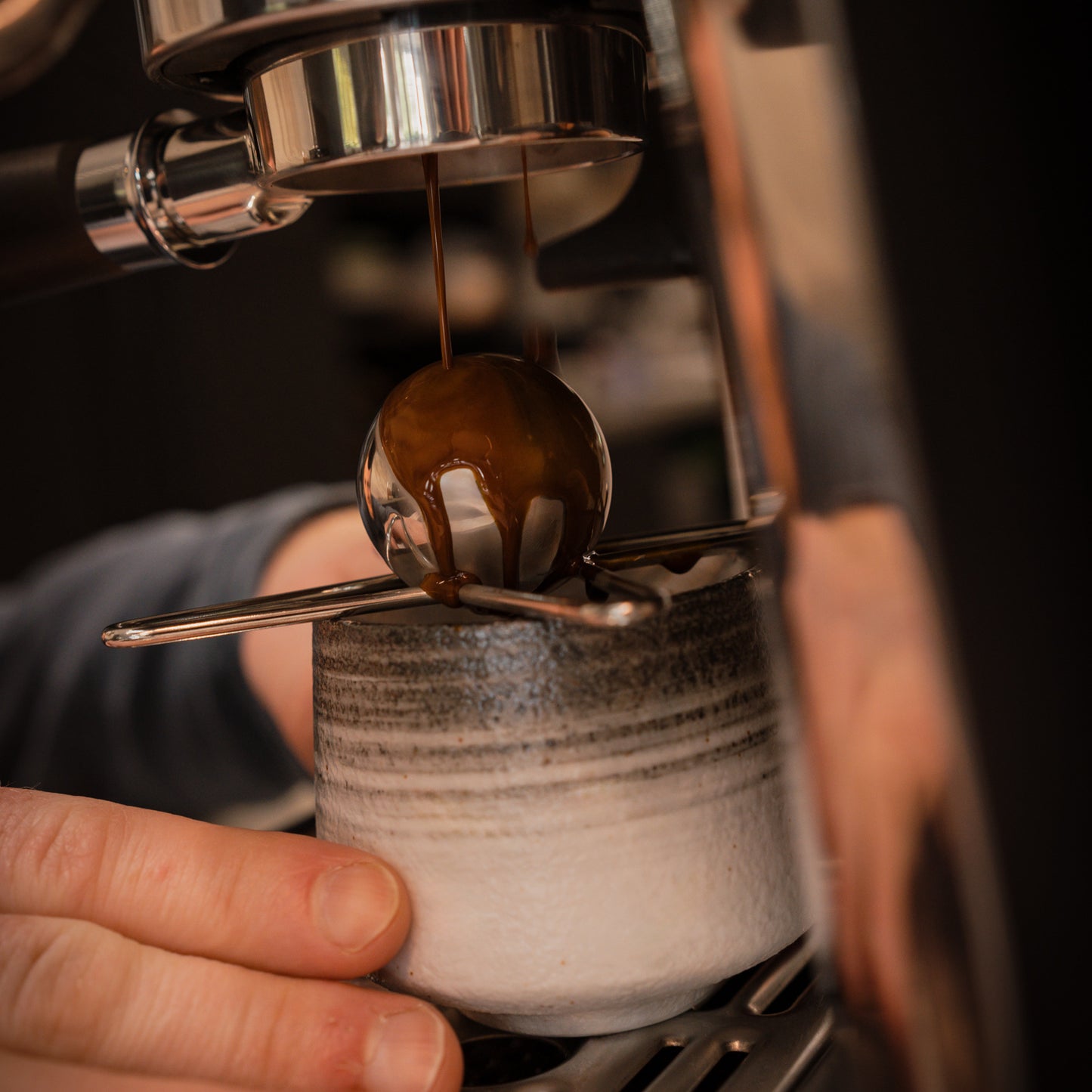 Close-up of an espresso machine pulling a shot with a mug underneath with a chilling ball atop.