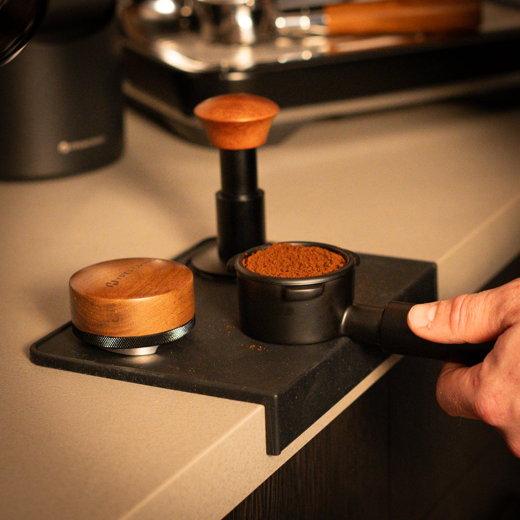Breville 54mm Bottomless Portafilter (Black) filled with coffee on a silicone tamping mat