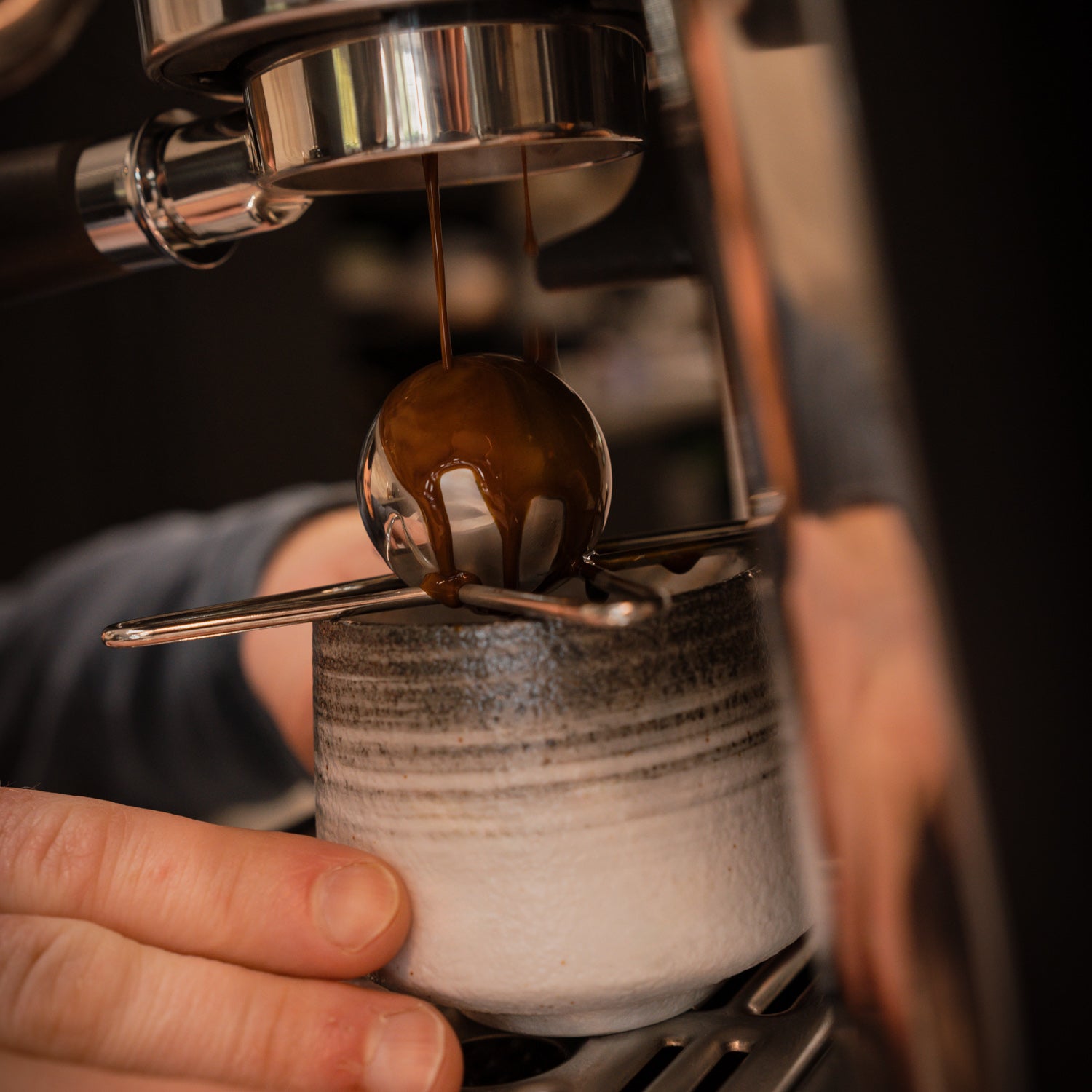 Close-up of an espresso machine pulling a shot with a mug underneath with a chilling ball atop.